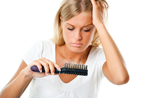 Женщина смотрит на расческу с выпавшими волосами